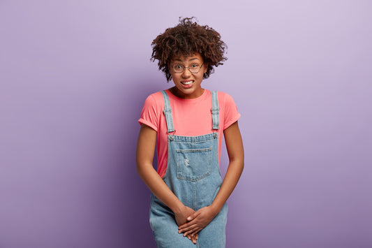 UTI unhappy-dark-skinned-woman-holds-crotch-needs-toilet-has-problematic-situation-wears-pink-t-shirt-denim-sarafan-suffers-from-cystitis-isolated-purple-wall-people-urgency